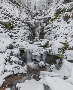 Scenic view of waterfall against snow covered rocks