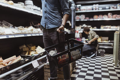 Midsection of male customer holding shopping basket at delicatessen shop