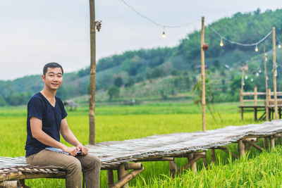 Portrait of man sitting on footbridge at field