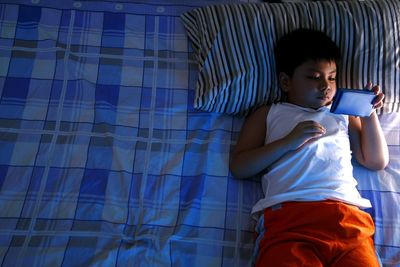 High angle view of boy using smart phone while lying down on bed at home