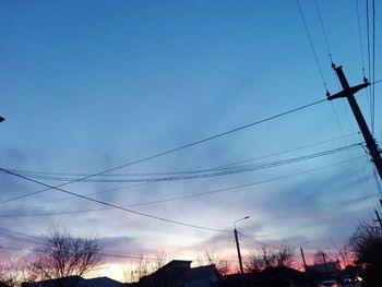 Low angle view of electricity pylon against sky at sunset