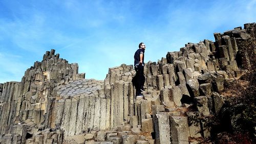 Low angle view of man standing on rock against sky