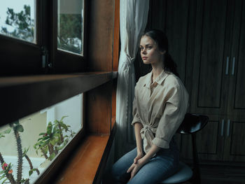 Portrait of young woman sitting on window