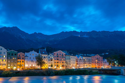 Illuminated buildings by lake against sky at night
