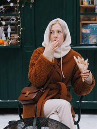 Young woman with blonde hair wearing brown fur coat eating sweet food on the christmas market.