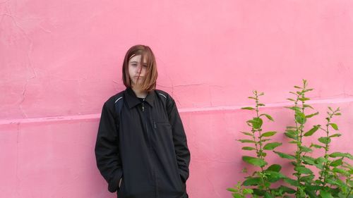 Portrait of teenage girl standing by plant against pink wall