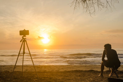Silhouette phone on tripod and man sit on beachchair during record vdo and photo beach 