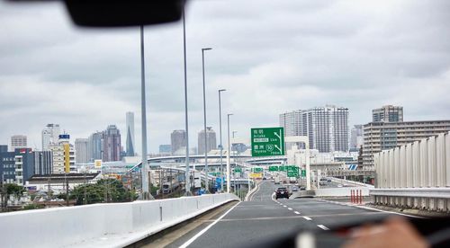 Road by modern city against sky