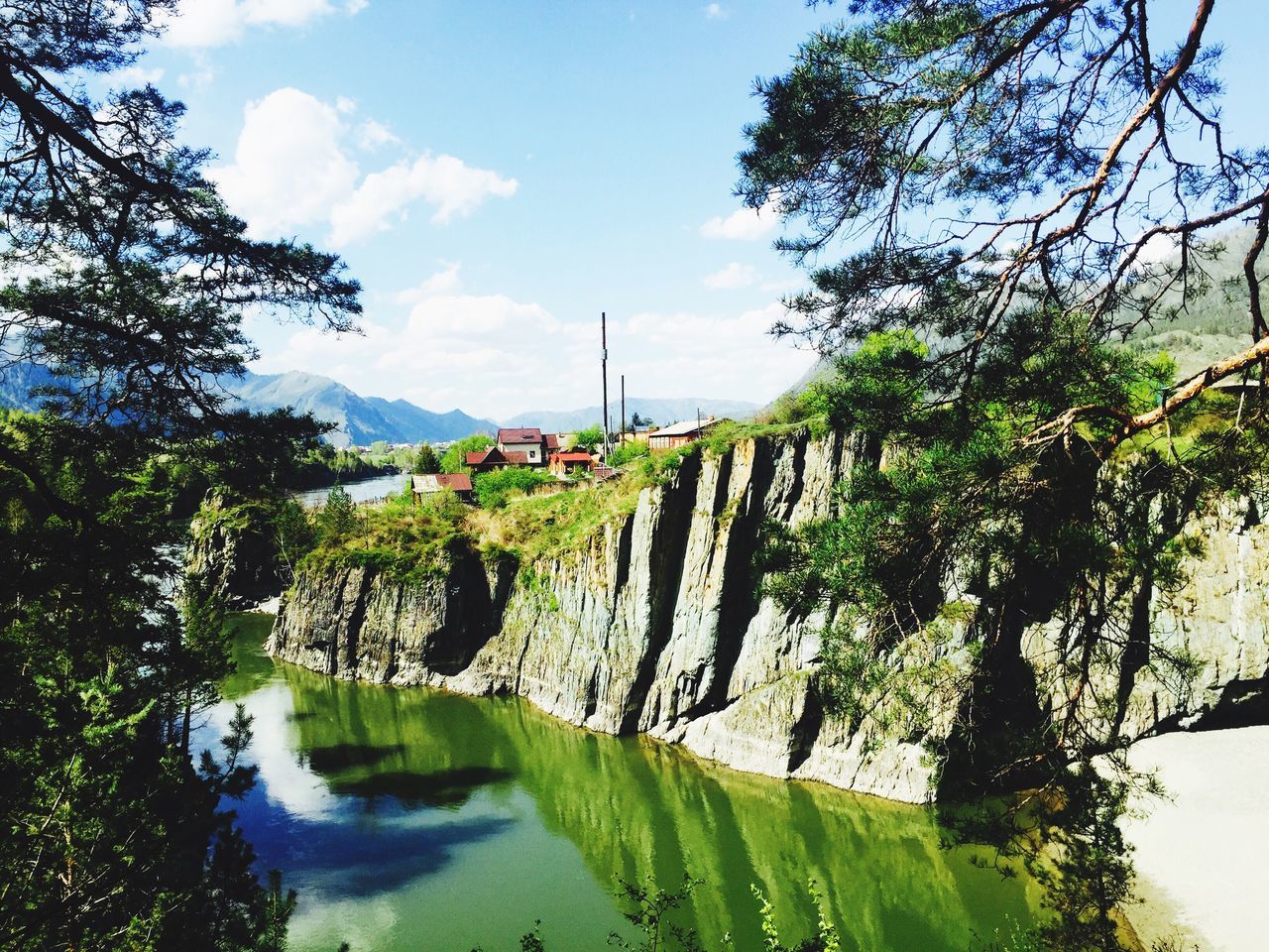 tree, water, sky, built structure, architecture, tranquility, river, green color, tranquil scene, building exterior, nature, scenics, cloud, beauty in nature, cloud - sky, reflection, lake, growth, day, waterfront