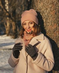 Portrait of woman standing by tree trunk during winter