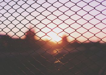 Close-up of chainlink fence against sky during sunset