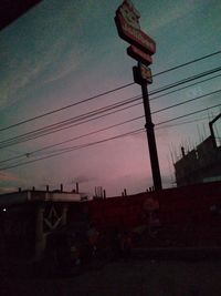 Low angle view of silhouette electricity pylon and building against sky