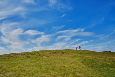 Two distant tourists walking on green hill