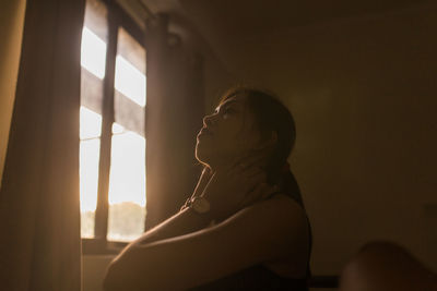 Portrait of young woman looking through window at home