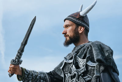 Low angle view of man in costume holding sword against sky