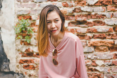 Portrait of beautiful young woman standing against brick wall