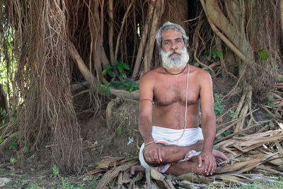 Portrait of shirtless man sitting on tree