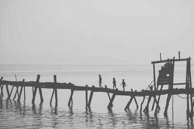 Silhouette children walking on pier over sea against sky