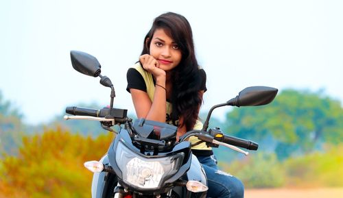 Portrait of young woman sitting on motor scooter against sky