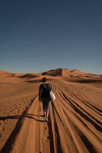 Rear view of woman walking at desert against clear blue sky