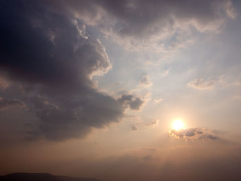 Low angle view of sunlight streaming through clouds during sunset