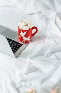Red christmas mug with marshmallows on top of hot chocolate on laptop.  festive holidays. high angle