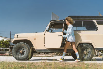 Young afro woman by old off-road vehicle on sunny day