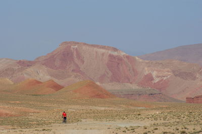 Rear view of man riding bicycle by mountains against clear sky