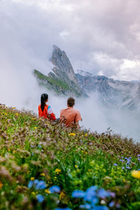 Rear view of men sitting on mountain against sky