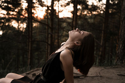 Side view of woman with eyes closed lying against trees in forest