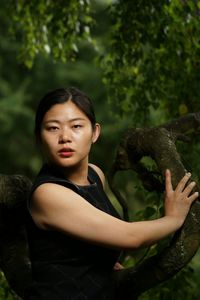 Portrait of young woman standing against trees