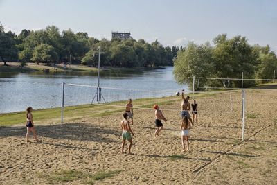 Friends playing volleyball on sand by lake against sky