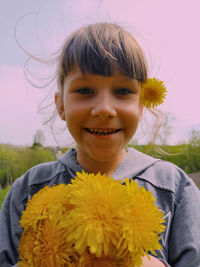 Close-up portrait of smiling girl holding flowers while standing against sky