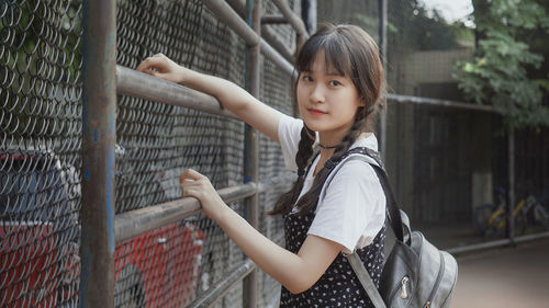 Portrait of young woman standing by fence