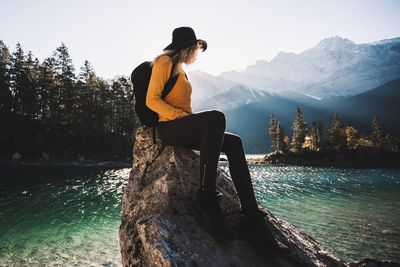 Woman sitting on rock by lake against mountains