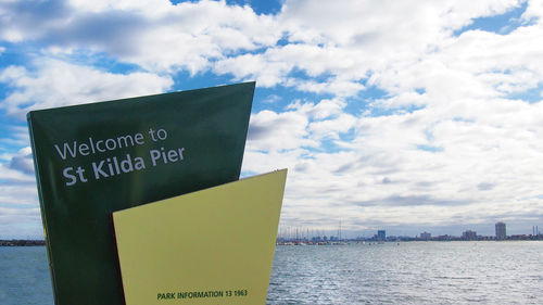 Close-up of information sign by sea against sky