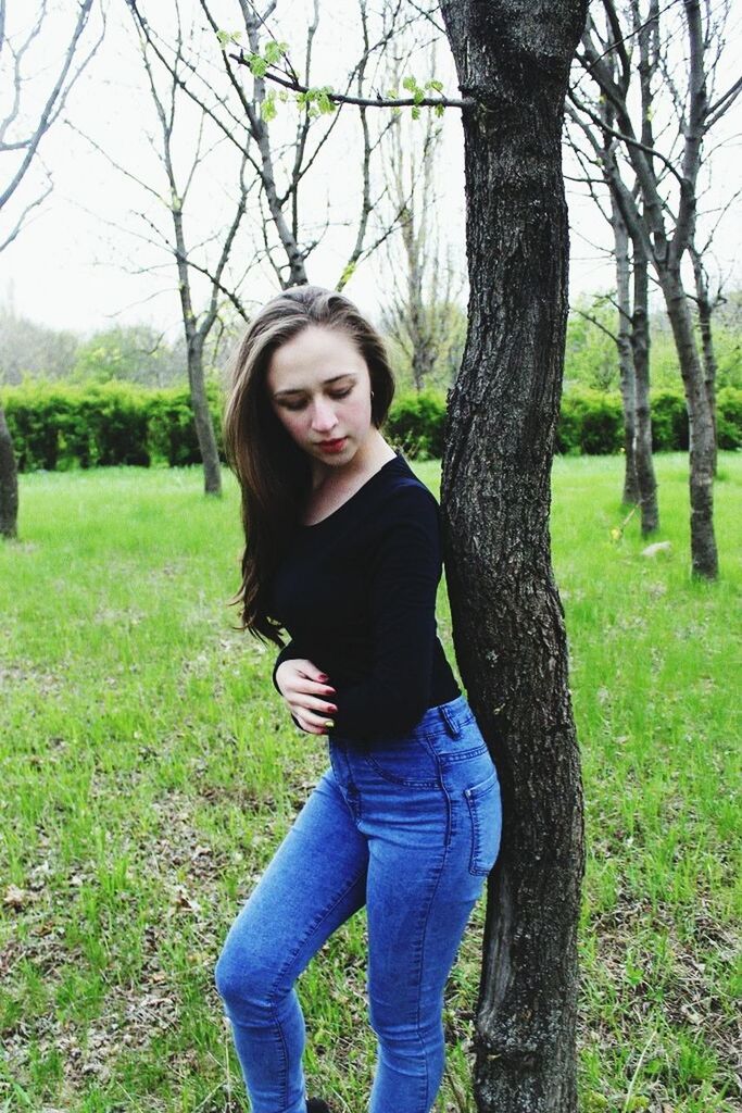 young adult, tree, young women, person, lifestyles, looking at camera, casual clothing, standing, portrait, front view, long hair, grass, leisure activity, three quarter length, tree trunk, smiling, field