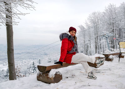 A girl sits on a wooden bench on top of a snow-capped mountain in the carpathians.