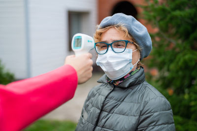 Cropped hand checking temperature of woman wearing mask