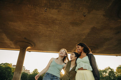 Cheerful teenage female friends enjoying under bridge