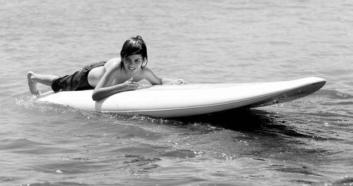 Full length of shirtless boy surfboarding in sea