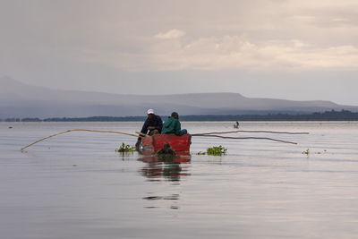 Rear view of people in boat at sea against sky