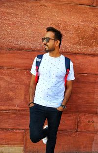 Young man looking away while standing against wall