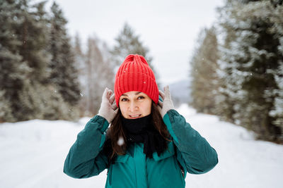 Portrait of smiling young woman wearing warm clothing standing on snow covered field