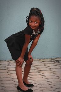 Portrait of smiling girl standing on footpath against wall