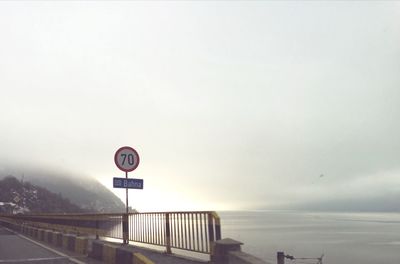 Road sign by sea against sky