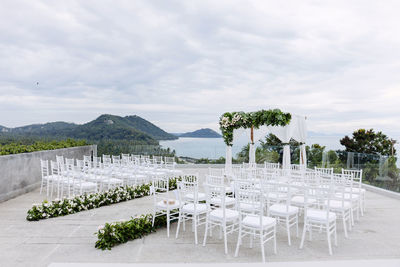 Empty chairs and table against trees against sky