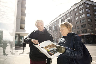 Senior couple reading catalog by building in city