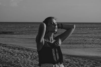 Portrait of young woman standing at beach against sky