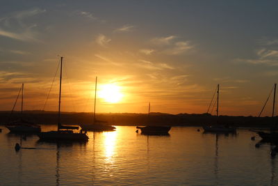 Sailboats moored on sea against sky during sunset